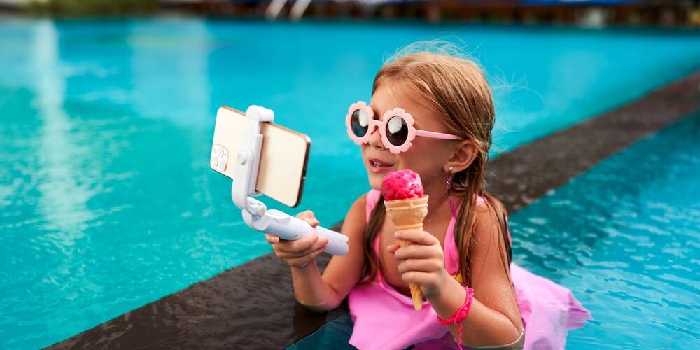 little,girl,in,pink,swimsuit,sits,in,pool,,holds,phone