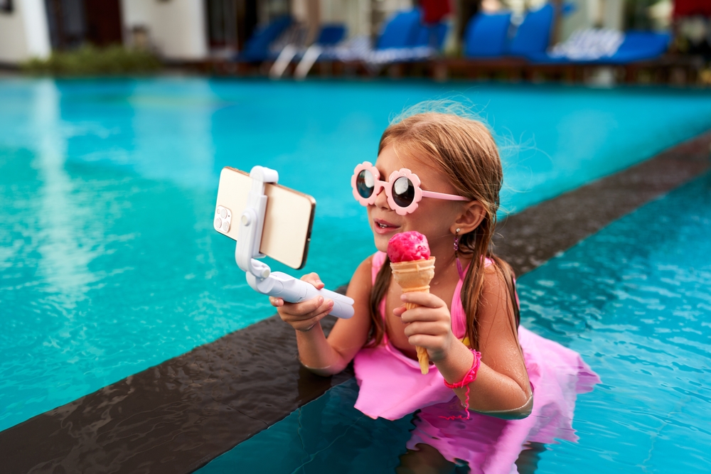 little,girl,in,pink,swimsuit,sits,in,pool,,holds,phone
